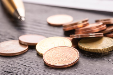 Stack of euro euro coins on old black wooden table. Pen and accounting documents with numbers