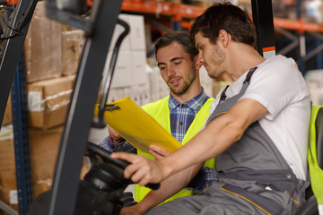 Concentrated loader and manager discussing goods and boxes they having to transport. Operator of...