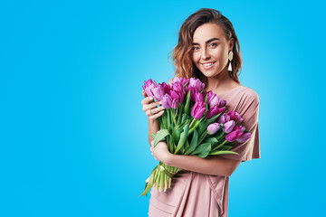 Young happy smiling redhead woman holding bouquet of purple tulips isolated on blue background. Festive bouquet in honor of women's day on March 8 or birthday