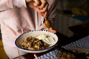 preperation of baked oatmeal with banana, blueberries, walnut and raisins. served with yoghurt and honey. dripping honey. putting yoghurt.