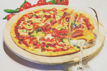 pizza with small sausages, basil, tomatoes and a glass of white wine on a white table, retro toned