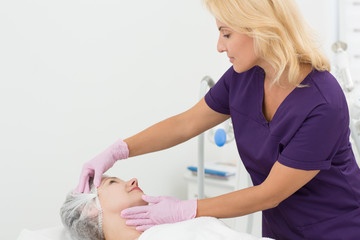 View from side of qualified beautician in process of examining skin of patient lying on couch. Female doctor in uniform and gloves in process doing hardware procedure. Concept of skin care and beauty.