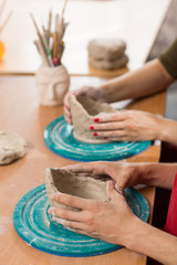 Crop of hands of woman and man sculpting bowls from clay on table in workshop. Process of doing earthenware in art studio. Concept of pottery art and ceramics.