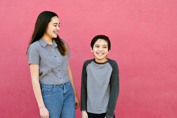 Brother and sister are having a fun time laughing and smiling while standing against the wall
