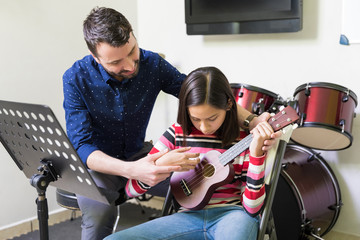 Trainer Assisting Teen Student In Playing Ukulele
