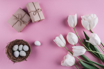 Easter eggs in nest and tulips flowers on spring background. Top view with copy space. Happy Easter card.