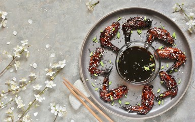 chicken teriyaki wings on a gray plate in a loft style on a concrete background and flowering plum twigs. Asian modern style. top view. copy space 