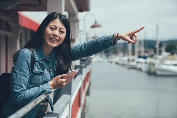 asian woman traveler use apps on mobile phone cheerfully standing on sife od port harbor wooden...