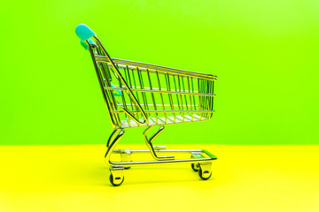 Miniature shopping cart on yellow green backdrop, retail shopping concept