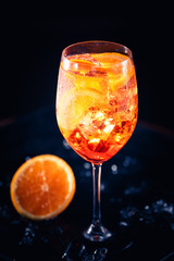 Stylish alcoholic aperol spritz cocktail with orange slice on black background.