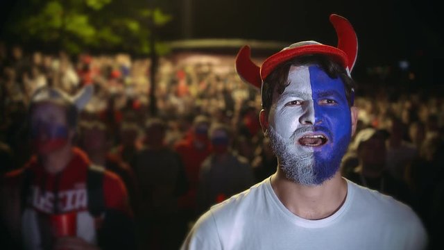 Football fan shouts, rejoices goal favorite 4K team. Person paint face jump in delight victory match. Closeup guy screaming furiously, jumping with friend against backdrop crowd winning football game