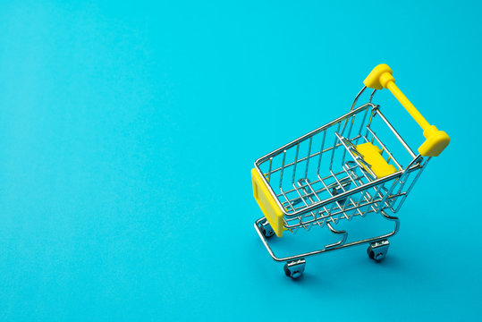 Shopping online or e-commerce modern lifestyle concept. Yellow supermarket trolley on blue background. Worldwide online shopping b2c e-commerce on internet website or social media at home.