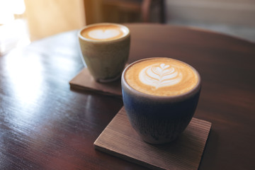 Closeup image of two small cups of hot latte coffee with latte art on vintage wooden table in cafe