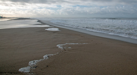 Serpentine shaped seafoam from Pacific ocean waves washing over the beach and flowing into a tidal marsh in Ventura California United States