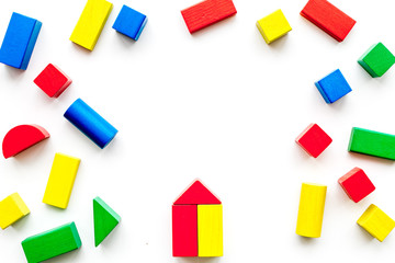 Construction game for kids. Wooden building blocks, toy bricks on white background top view copy space frame