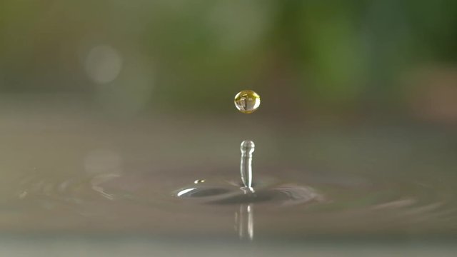SLOW MOTION, MACRO, DOF: Yellow droplet of sunflower oil falls into a sink full of water. Detailed slow motion shot of a shiny drop of oil creating a ripple after falling into a body of cold water.