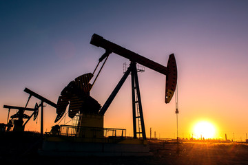 Oil pumps are running in the sunset at the oil field. The outline of the pumping unit.