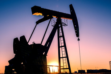 Oil pumps are running in the sunset at the oil field. The outline of the pumping unit.
