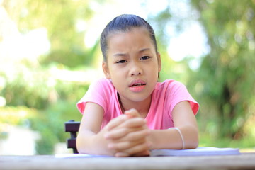 Asian little girl reading a book and sitting on desk at home.Does not want to do boring reading a book.