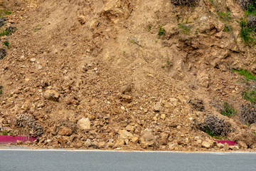 Landslide debris on rural road from steep slope after winter rain storm. Scattered pieces of rock slide debris cover red curb on road