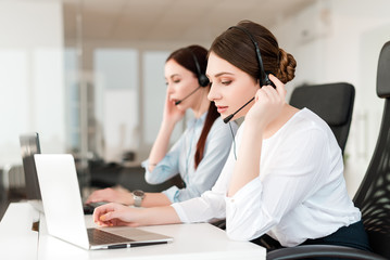 Friendly young female technical support dispatcher with a headset working in a call center on a...
