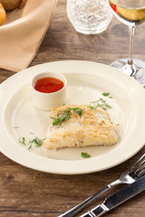 Baked cod fish fillet with sauce on the side on wooden table