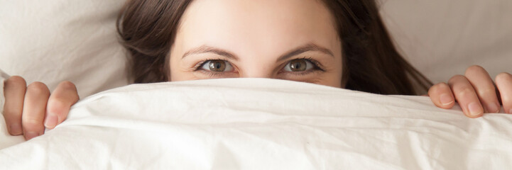 Horizontal image woman hiding under white blanket lying on pillow