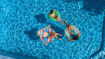 Family in swimming pool aerial drone view from above, happy mother and kids swim on inflatable ring donuts and have fun in water on family vacation, tropical holidays on resort