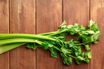 An overhead photo of fresh organic celery stalks with leaves on a dark rustic wooden background with a place for text
