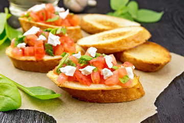 Bruschetta with tomato and cheese on dark board