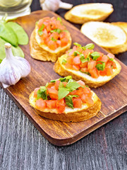 Bruschetta with tomato and spinach on dark wooden board
