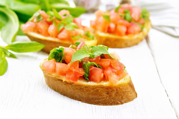 Bruschetta with tomato and spinach on light wooden board