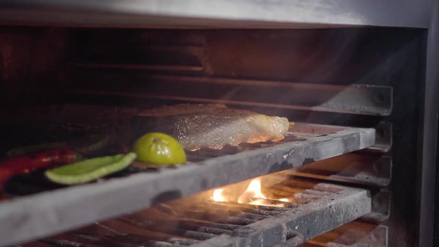 Inside charcoal oven for grilling are cooked salmon fish, lemon, bell pepper and chilli