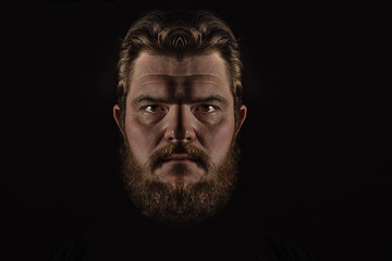 Fototapeta premium Close-up portrait strong serious brutal bearded man on black. Confident and dramatic concept