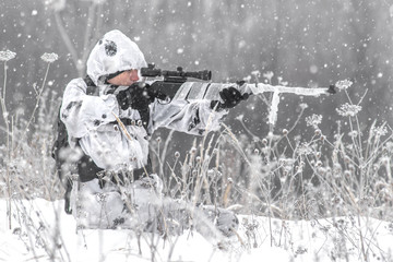 Man soldier in the winter on a hunt with a sniper rifle in white winter camouflage aims sitting in...