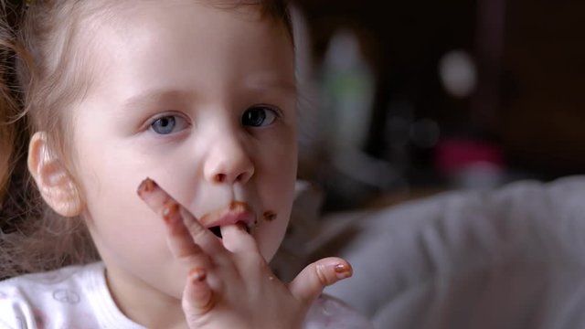 Child licking chocolate off her fingers. Funny small girl eating chocolate.