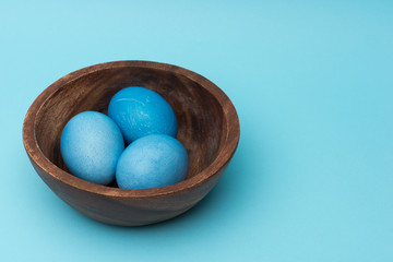 Painted easter eggs in the round wooden plate on blue background, monochrome view