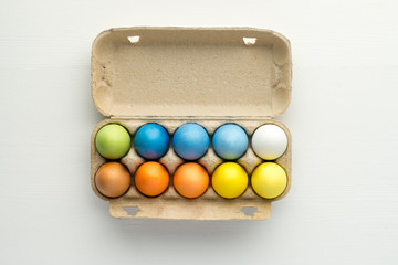 Pastel painted easter eggs in the box on white wooden background, top-view