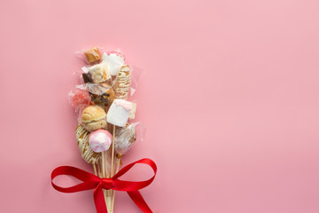 Bouquet of different candies with red ribbon on pink background, top-view