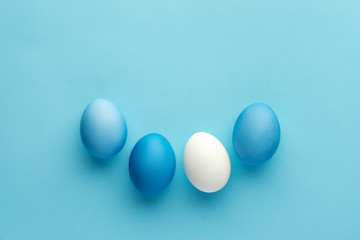 Blue painted eggs with white natural egg on blue baackground, monochrome top-view