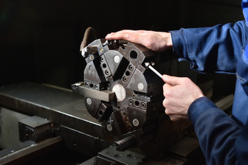 A worker in blue workwear performs maintenance on the CNC machine to install drills in the turret for working with metal. Hands of the worker close up, screw various drills © pridannikov
