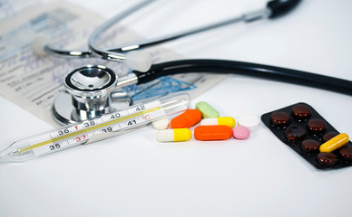 bunch of different drugs, vitamins, antibiotics and tablets lie on a white background with a phonendoscope, thermometer and prescription form