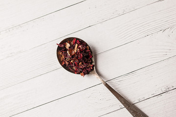 Dry tea with fruit, rosehip, rose in a spoon on a white wooden background close-up