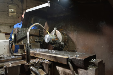 The worker in blue workwear, the operator of the CNC machine, oversees the process and controls it. A man works in a factory with CNC machine