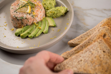 Frau isst rohes Lachstatar mit Lachs, Dill, Zitrone, Avocado und Vollkorn Toast Brot auf Porzellan...