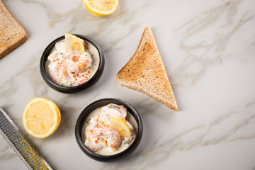 Garnelen Salat mit Lachs Kaviar,  Kräuter, Zitrone, und Vollkorn Toast Brot in schwarzer Schale auf Marmor Hintergrund