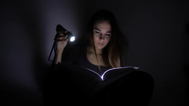 close-up portrait girl is reading a book with a flashlight in a dark room at night. 4k. Motion shooting