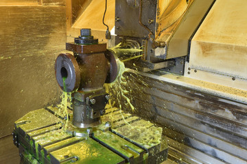 The process of drilling and grinding holes in the body of the valve on the CNC machine. Yellow-green coolant splashes into place