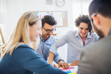 Group of young businesspeople sitting around table in a modern office, having meeting.