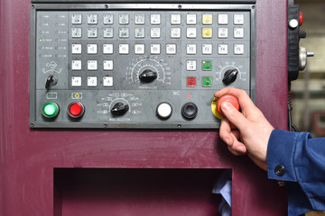 Worker in blue workwear holds hands on the control panel of the CNC machine. Close-up